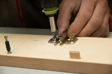 The furniture maker assemble a wardrobe, he is tightening the screws rechargeable screwdriver.