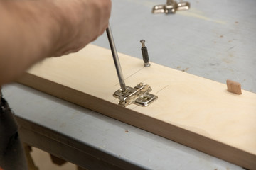 The furniture maker assembles the Cabinet, he tightens the screws with a screwdriver .