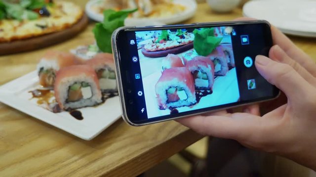 close-up. Female hands take a photo of sushi on a smartphone in a restaurant.