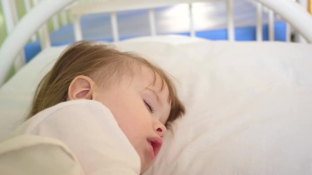small child is sleeping on pillow. close-up. Charming baby falls asleep on white bed in his bed in room at home. concept of sleeping child.