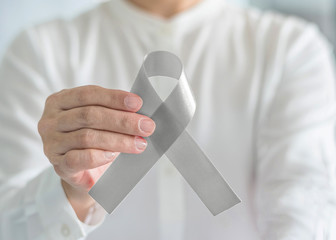 Silver color ribbon awareness on person's hand for Parkinson's disease, Brain cancer, Schizophrenia, Sciatic Pain and Brain disorder or disability illness