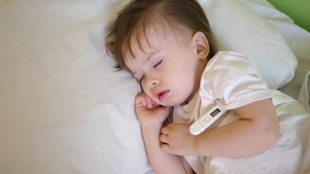 sick child with thermometer sleeping on white bed. temperature of child is measured using thermometer in hospital ward.
