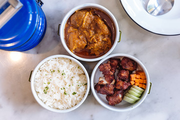 Thai food meal: Stream rice with parsley, Hang Lay Pork Curry and Stir fried spare rib pork with carrot and cucumber served in food carrier.