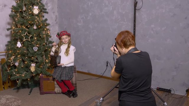 Photographer taking picture girl teenager with lantern on Christmas tree background. Girl teenager posing in New Year photo studio at holiday photo session. Backstage in studio