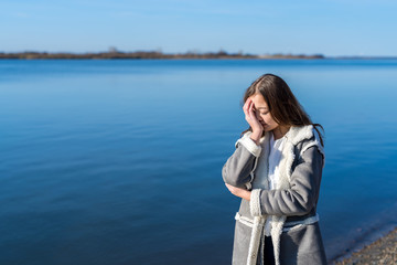 Fototapeta premium The girl in the sheepskin coat is crying on the river bank