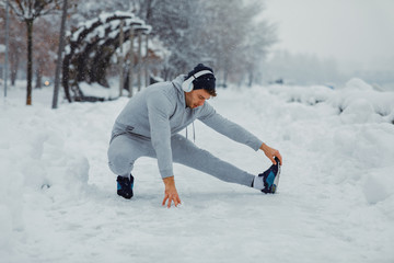 Young man stretching legs on snowy day in the city