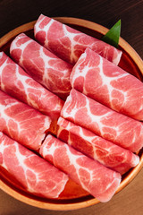 Close up Premium Rare Slices Kurobuta (Black Pig) pork with low-marbled texture on circle wooden plate served for Sukiyaki and Shabu.