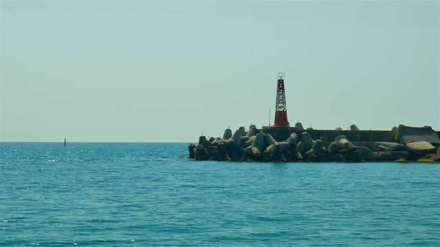 Pier of the sea port with lighthouse. Blue water. Sunny day.