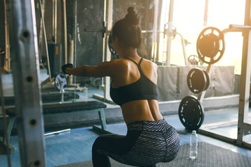 Rear view of young asian woman in sportswear doing squat at health club.