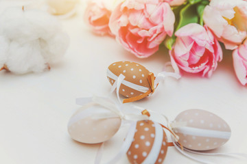 Spring greeting card. Easter eggs with moss cotton and pink fresh tulip flowers bouquet on rustic white wooden background. Easter concept. Flat lay top view copy space. Spring flowers tulips