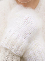 Closeup view of female hands wearing white fluffy cozy knitted mittens while standing outdoors on cold frosty winter day. Vertical color photography.