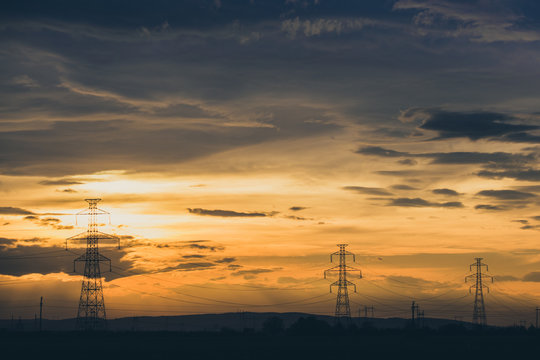 High voltage electic pylon line on party cloud sunset