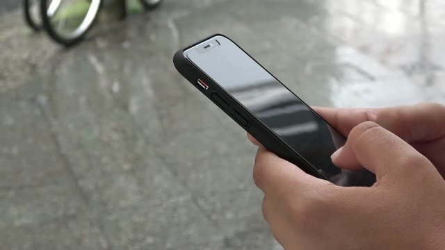 Berlin, Germany-11 July, 2018: 4K. Business person using his smartphone while it is raining. Sending messages or email. Close-up of hands typing on the phone. The raindrops fall on the ground