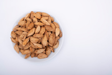 Almonds with shells and they are in white porcelain bowl