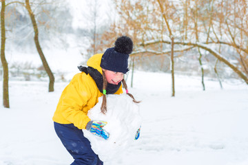 Fototapeta na wymiar little girl sculpts snowman. the kid is carrying a lump of snow