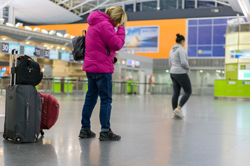 Young woman with hand luggage in international airport terminal, looking at information board, checking her flight. girl with a suitcase at the airport.