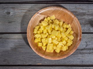 Diced raw potatoes in a deep plate. Shot from above on a wooden old table. Close-up.