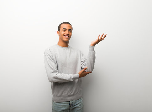 African american man on white wall background extending hands to the side for inviting to come