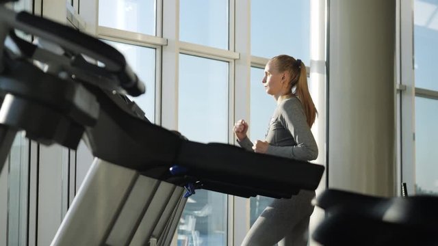 Attractive woman of middle age is running on tread mill in sport gym