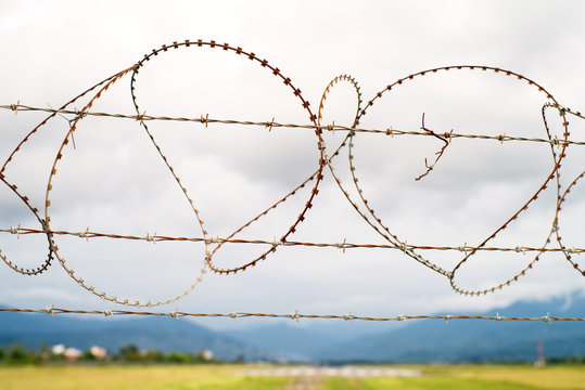 Fence from a barbed wire against the background of a runway of the airport and mountains