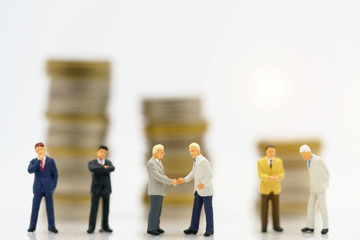 Miniature people: Businessman handshake to business success with coins stack. Commitment, agreement, investment and partnership concept