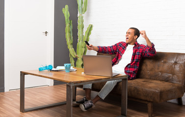 African american man with laptop in the living room with a television remote