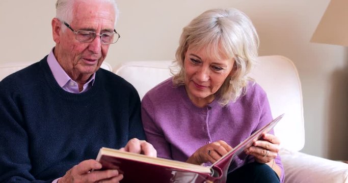 Senior Couple Sitting On Sofa And Looking At Photo Album Together
