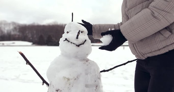 4K Footage of happy young girl standing on the street and sculpts a snowman, smile to camera. - Video