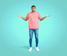 Standing young african american man having doubts and with confuse face expression while raising hands and shoulders on colorful background