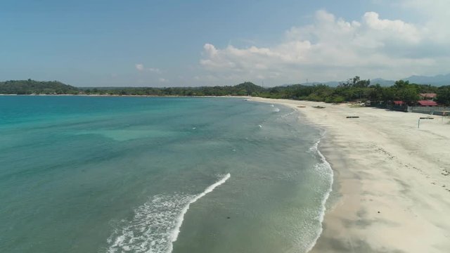 tropical beach Cabugao with white sand and palm trees in the Philippines, Luzon. Aerial view coast with beach and turquoise water.