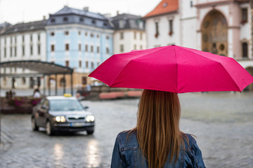 Young woman with umbrella waiting for taxi car on the street in rain