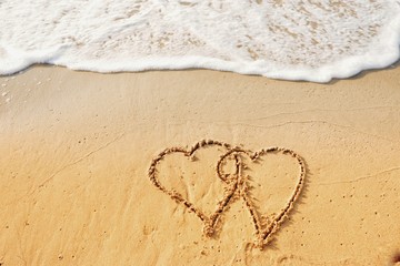 Valentine's day concept, two heart shape writing on sand beach with waves ocean.