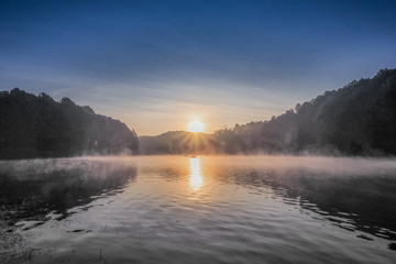 sunrise at Pang Oung, beautiful lake view misty morning of soft mist moving on the water with reflection of pine forest on water and colorful of sun light in the sky background, Mae Hong Son, Thailand - obrazy, fototapety, plakaty