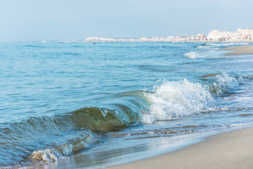 Fototapeta na wymiar Waves with foam on the sea green color, long sandy beach.