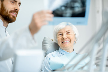 Happy elder woman during the consultation with handsome dentist showing panoramic x-ray in the dental office - Powered by Adobe