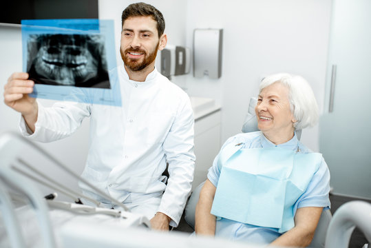 Happy elder woman during the consultation with handsome dentist showing panoramic x-ray in the dental office