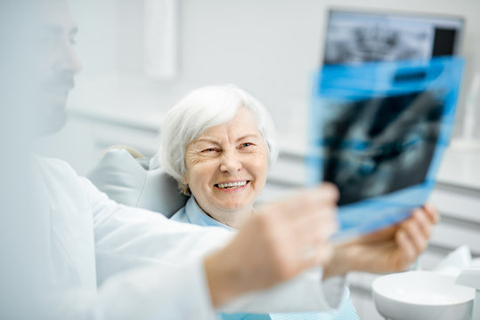 Happy elder woman during the consultation with handsome dentist showing panoramic x-ray in the dental office