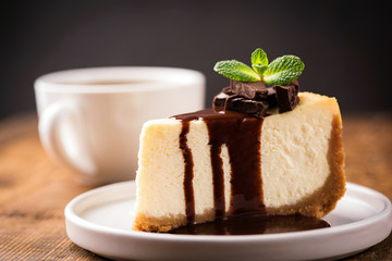 Cheesecake with chocolate sauce on plate served with cup of coffee. Closeup view. Tasty delicious cake