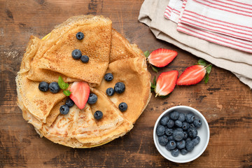 Crepes, thin pancakes or russian blini with fresh berries on rustic wooden background. Table top view