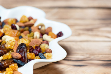 Mix of nuts and berries. Dried fruits in white plate on wooden table, copy space for text. Healthy food and vitamins