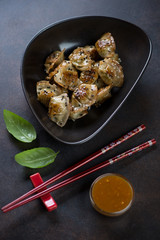 Black bowl with fried korean wontons and sesame seeds, studio shot on a brown metal background