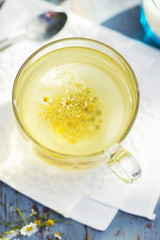 Fresh chamomile blossom tea in a glass cup on a wooden table, healthcare and healthy eating concept