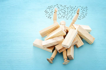 wooden dummy buried under stack of domino blocks asking for help. concept of stress, trouble and deadline overwork.