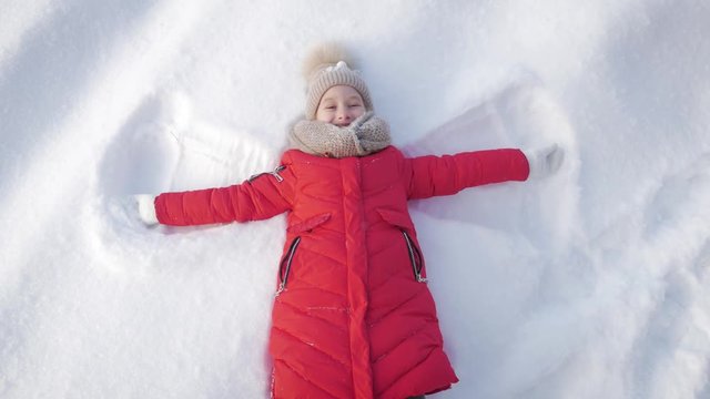 Happy girl lying on a snow and shows angel. A pretty girl in a coat lies on the snow, spreading her arms.