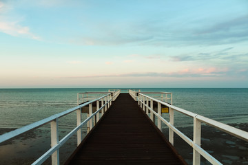 Wooden pier during sunset overseeing the ocean with orange clouds and turquoise sky (Hervey Bay near Fraser Island, Queensland, Australia)