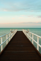 Close-up of wooden pier during sunset overseeing the ocean with orange clouds and turquoise sky (Hervey Bay near Fraser Island, Queensland, Australia)