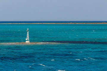 Small lighthouse in a little island in the turquoise water. Small waves. Bright summer day.