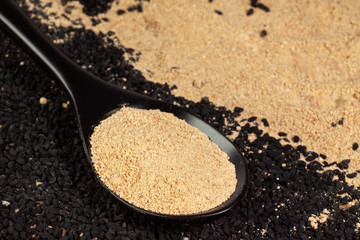 Ginger powder in spoon on black cumin (nigella sativa or kalonji) seeds background