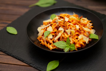Tasty appetizing classic Italian Fusilli pasta with tomato sauce, cheese Parmesan, beef and basil in black bowl on table. 