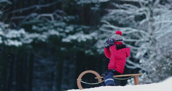 CU Cute little kid boy child preparing for a sledge ride down the hill. Child plays outdoors in snow, winter fun. 4K UHD 60 FPS SLOW MOTION 